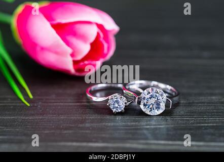 Close up Diamond gem wedding rings with pink tulip flower on black background Stock Photo