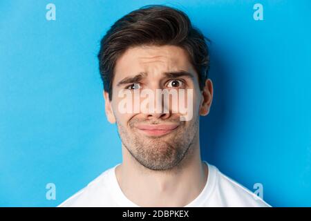 Head shot of skeptical and disappointed man, grimacing complicated, standing against blue background Stock Photo