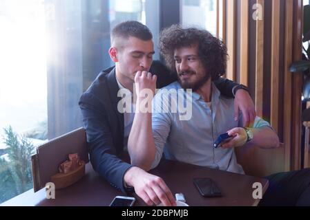 Two gay male friends hugging in a cafe, smiling and having a cigarette. LGBT and love concept. Stock Photo