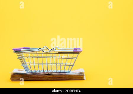 On the bundle of notes lies an empty grocery basket Stock Photo