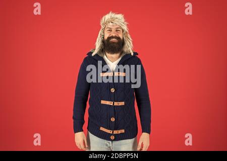 Fashion menswear shop. Masculine clothes concept. Winter menswear. Clothes design. Man bearded stand warm jumper and hat on red background. Winter season menswear. Hipster rustic style furry hat. Stock Photo
