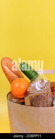 Paper bag with food supplies for the period of quarantine isolation on a yellow background. Delivery, donation, coronavirus. Copyspace. Buckwheat past Stock Photo