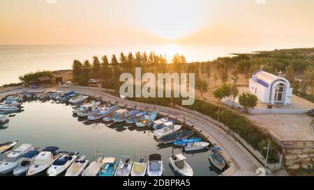 Aerial view of coastline sunset and landmark white washed chapel at Agia Triada beach, Protaras, Famagusta, Cyprus from above. Bird's eye view of tour Stock Photo