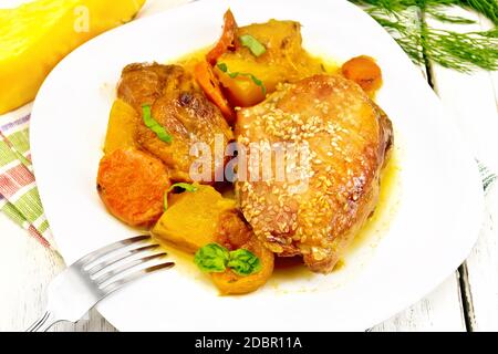 Chicken stew with pumpkin, dried apricots, carrots and red wine, sprinkled with sesame seeds in a dish on a kitchen towel against white wooden board