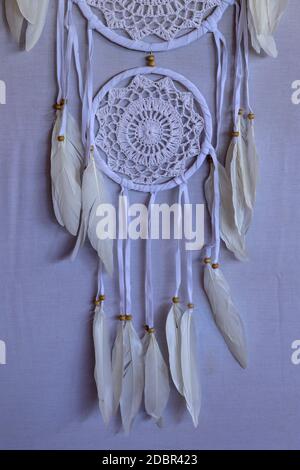 Handmade pink dream catcher with white doily on background of rocks and lake. Tribal elements, feathers, lace, crochet snowflake. Stock Photo