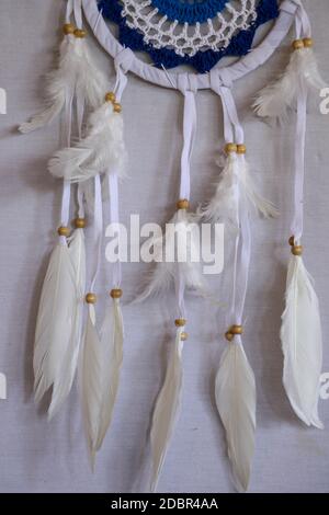 Handmade pink dream catcher with white doily on background of rocks and lake. Tribal elements, feathers, lace, crochet snowflake. Stock Photo