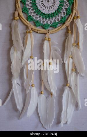 Handmade pink dream catcher with white doily on background of rocks and lake. Tribal elements, feathers, lace, crochet snowflake. Stock Photo