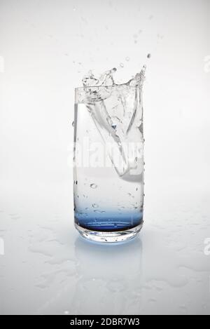 An ice cube dropping into a glass of water creating a splash. The blue ...