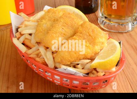 Fish and chips served in a basket wrapped in newsprint with a mug of beer Stock Photo