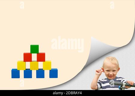 Smiling blond boy in bent corner of the page and colorful pyramid of wooden cubes on orange blank paper ready for your use. Stock Photo