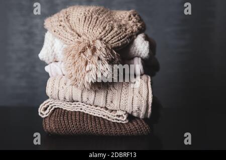 Winter woolen cap on sweaters piles on a desk at home. Clothes for winter and cold day concept. Copy space for design or text Stock Photo