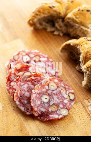 Sliced italian salami with hazelnuts and bun on wooden table. Stock Photo