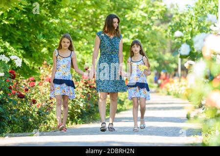 young woman walks down the path in the flowering garden by the hand with her two daughters Stock Photo
