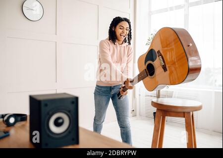 Crazy woman breaks the guitar near audio speaker, the music is maddening. Pretty lady relax in the room, female sound lover resting Stock Photo