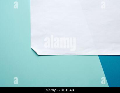 white blank sheet of paper with curled corner on a blue background, copy space Stock Photo