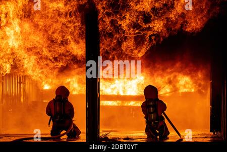 Firefighters using water fog fire extinguisher to fighting with the fire flame in large building. Firefighter and industrial safety disaster and publi Stock Photo