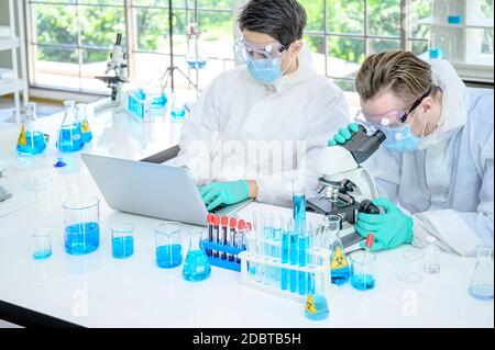 Couple male scientist wearing protection suit working with Microscope and computer laptop and many lab equipment for research Coronavirus  vaccine at Stock Photo