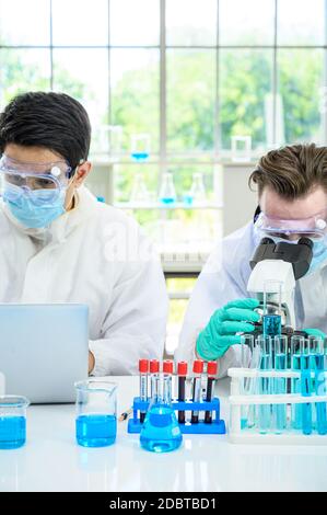 Couple male scientist wearing protection suit working with Microscope and computer laptop and many lab equipment for research Coronavirus  vaccine at Stock Photo