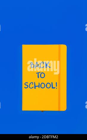 Back to school handwritten sign on yellow leather cover notebook over blue paper background with copy space Stock Photo