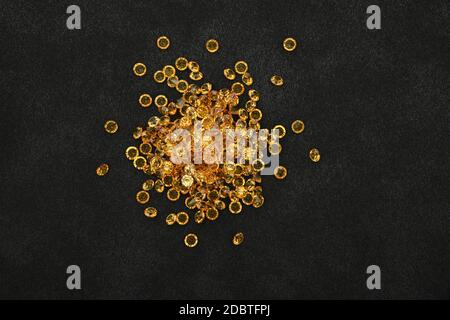 Close up heap of golden yellow rhinestone crystals over black leather background, elevated top view, directly above Stock Photo