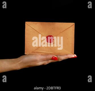 Woman hand palm with red nails holding and presenting old sealed brown paper paper envelope over black background, side view Stock Photo