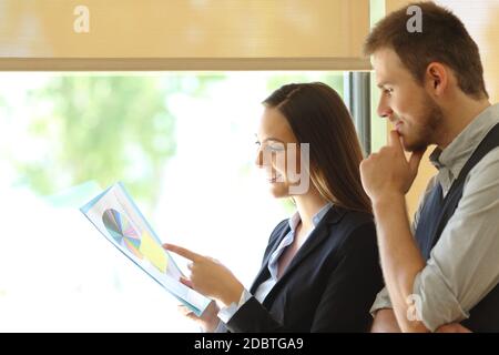 Two executives analyzing graph report document standing by the window at the office Stock Photo