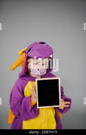 beautiful and young girl with nose and mouth mask dressed as dragon holding blackboard Stock Photo