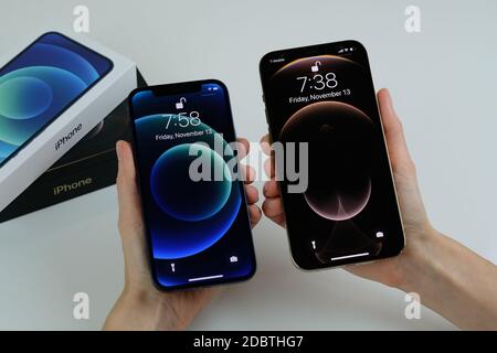 iPhone 12 Pro Max in Gold next to iPhone 12 in Blue on a white desk Stock Photo