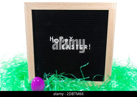 A Black Sign With a Birch Frame That Says Happy Easter in White Letters With a Purple Easter Egg and Green Easter Grass in Front of It on a Pure White Stock Photo