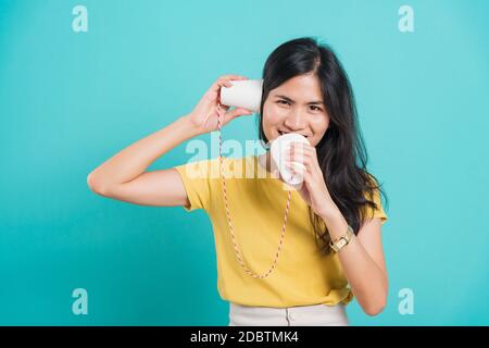 Portrait happy Asian beautiful young woman smile white teeth standing wear yellow t-shirt, She holding paper can telephone for talking, studio shot on Stock Photo
