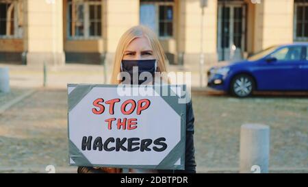 Concerned woman in protective mask with protest banner calling to stop hackers by walking on the city street Stock Photo