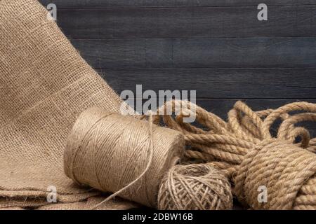 Two spools of burlap threads or jute twine and coil of linen rope on sackcloth fabric in close-up on grey background Stock Photo