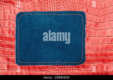 Blank jeans frame. Denim patch with orange thread seam on red skin. With space for design, text place. Stock Photo