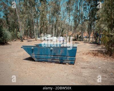 Large blue metallic garbage bin at a camping site in Jordan Valley of Israel. Many tents near the Eucalyptus trees in the background. Adventure vacati Stock Photo