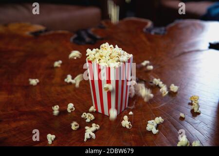 Popcorn flying out of cardboard box. red and white striped popcorn bucket with flying popcorn in the living room, movie or cinema concept food or snac Stock Photo