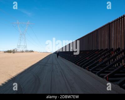 Woman walking along USA and Mexico border wall with diagonal shadow Stock Photo