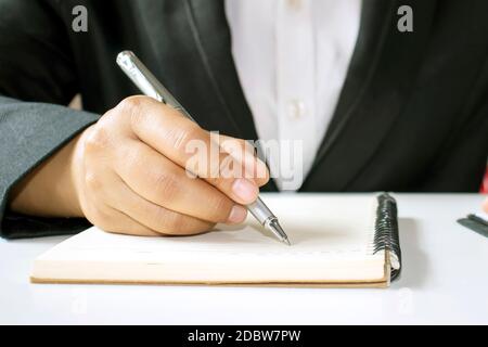 Close-up of a businesswoman wearing a black dress using a pen to write a notebook or document. Stock Photo