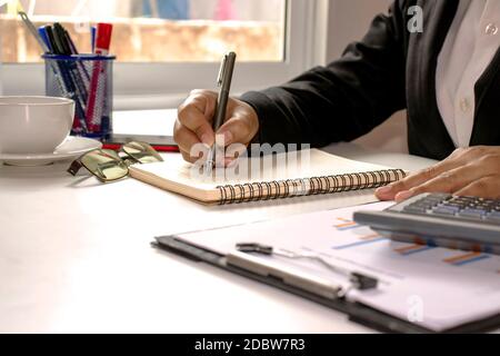 Business people are using a pen to take notes, including calculators and financial reports on the desk. Stock Photo