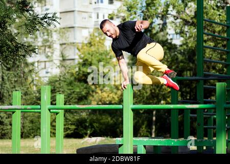 The young guy is jumping and doing street workout and parkour outdoors in park. Stock Photo