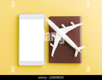World Tourism Day, Top view flat lay of minimal toy model plane, airplane on passport and mobile smartphone blank screen, studio shot isolated on a ye Stock Photo
