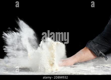 chef in black uniform sprinkles white wheat flour in different directions, product scatters dust, black background, particles scatter and freeze in th Stock Photo