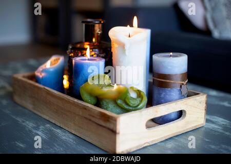 Various colored burning candles on wooden table in modern home, in wooden retro box, cozy style interior decoration beauty Stock Photo