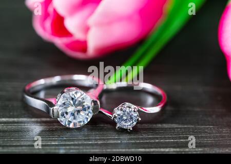 Close up Diamond gem wedding rings with pink tulip flower on black background Stock Photo