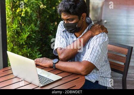 Closeup back the Asian black man use hand holding chiropractor shoulder really bad neck pain from using laptop computer he working long time, Injury o Stock Photo