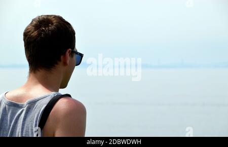 Young man in singlet and sunglasses looking at the Japanese sea. Much copy space Stock Photo