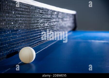Closeup one white ball on the blue ping pong table with a black net, Table tennis paddle is a sports competition equipment indoor activity and exercis Stock Photo