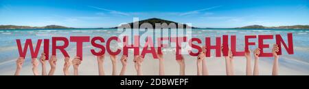People Hands Holding Colorful German Word Wirtschaftshilfen Means Economic Aid. Ocean And Beach As Background Stock Photo