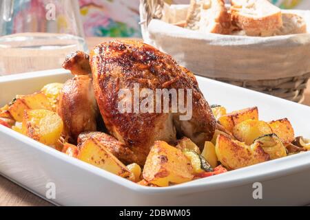 Selective focus of a delicious looking spit-roasted chicken with baked potatoes and vegetables on a baking dish. Traditional food concept. Stock Photo
