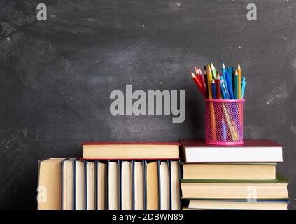stack of various books, stationery on black chalk board background, back to school, copy space Stock Photo