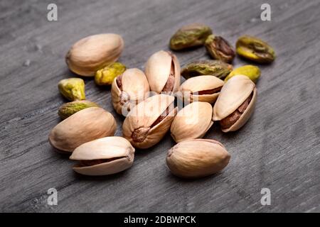 Pile of roasted pistachio nuts (Pistacia vera) in shell and seeds on dark gray wood table Stock Photo
